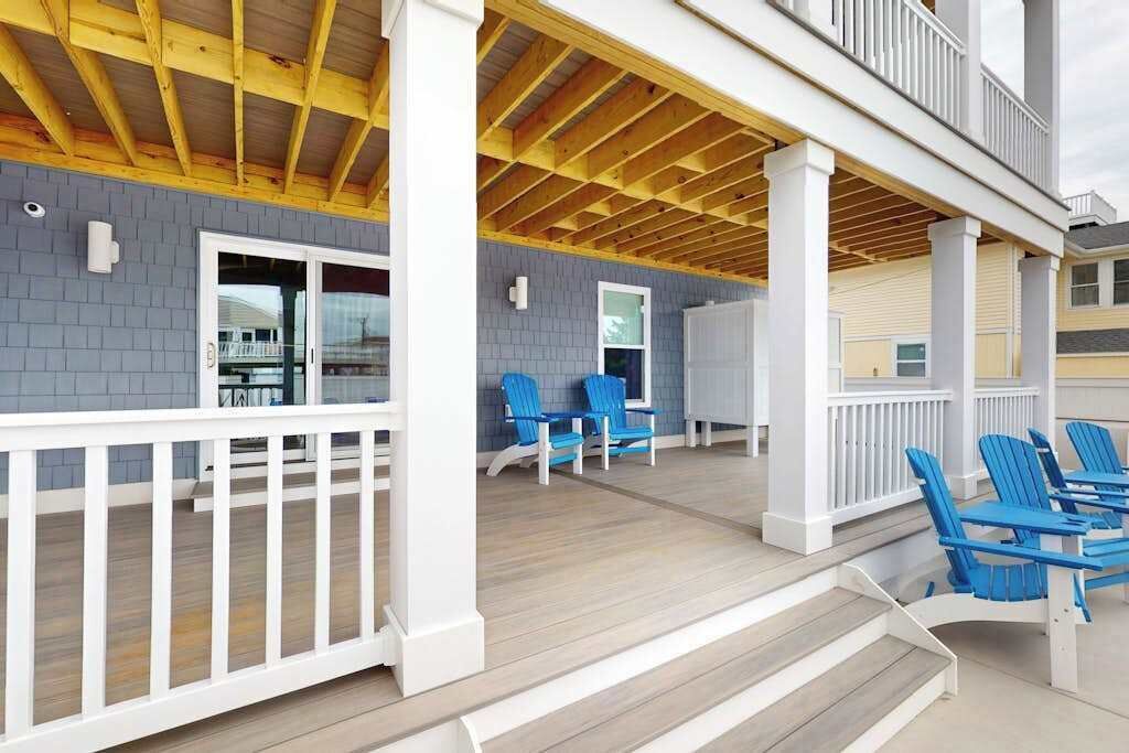 A covered outdoor area with a wooden deck, blue chairs, and a white railing.