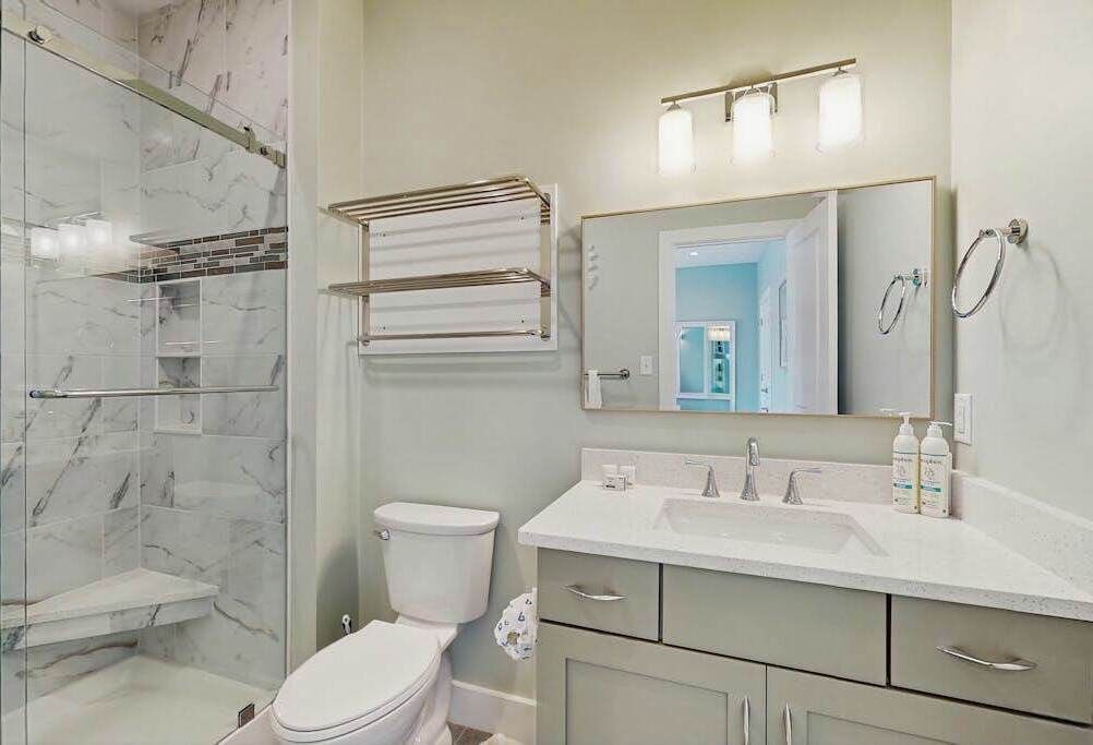 A bathroom with a glass shower enclosure, a toilet, a sink with a mirror above it, and a towel rack.