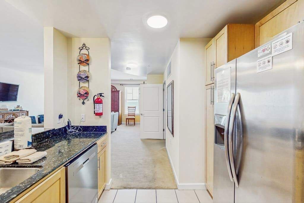 A kitchen with a stainless steel refrigerator, wooden cabinets, a marble countertop, and a hallway leading to a dining area.