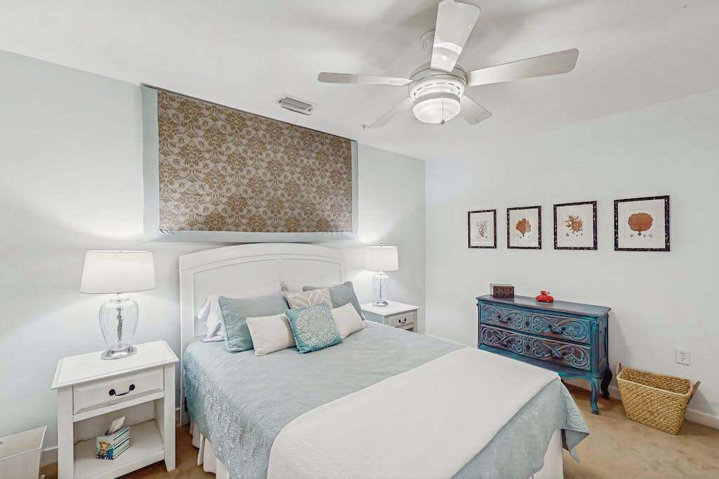 A bedroom with a bed, nightstands, a dresser, a ceiling fan, and framed pictures on the wall.