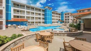 Ein Hotel mit mehreren Etagen, Außenpools und einer Terrasse mit Tischen und Stühlen.