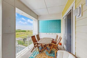 A balcony with a table and chairs, a view of the landscape, and a blue tiled wall. - Cozy condo close to beach with AC, W/D, fitness room & pool (Virginia Beach)