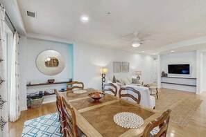 A dining area with a wooden table, chairs, and a round mirror on the wall. - Cozy condo close to beach with AC, W/D, fitness room & pool (Virginia Beach)