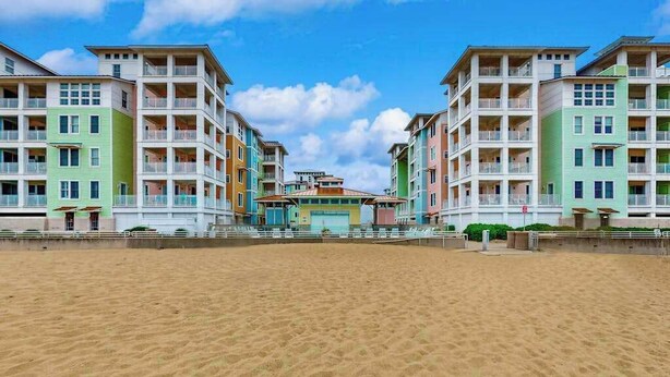 Ein Strandhotel mit mehreren Etagen, Balkonen und einem zentralen Gebäude mit Dach.