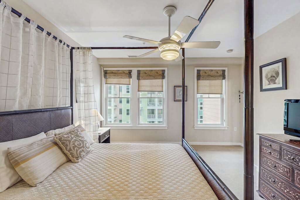 Quarto com cama, ventoinha no teto, janelas e cômoda.