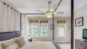 Ein Schlafzimmer mit Bett, Deckenventilator, Fenstern und einem Schminktisch.