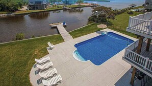 A swimming pool with lounge chairs, a dock, and a view of a body of water. - Fully-equipped canal-front home w/private outdoor pool, bay, dock, and views (Virginia Beach)