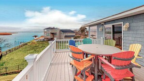 A deck with a table and chairs, a view of the water, and a building with a porch. - Fully-equipped canal-front home w/private outdoor pool, bay, dock, and views (Virginia Beach)