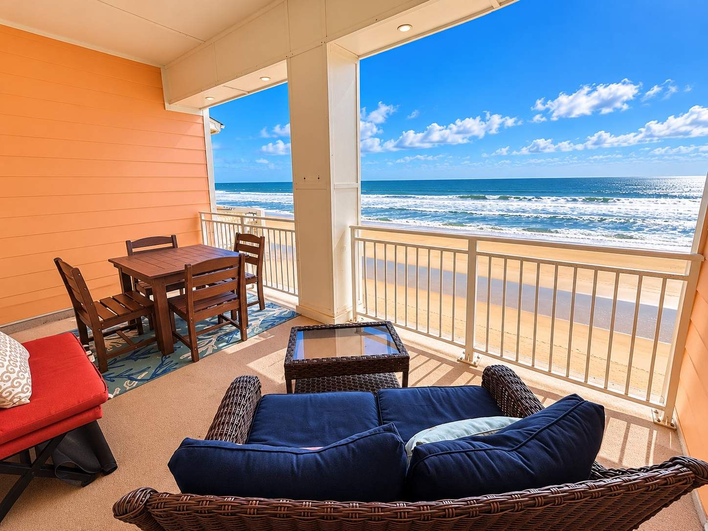 A balcony with a view of the ocean, a dining table, chairs, and a sofa.