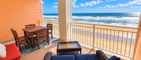 A balcony with a view of the ocean, a dining table, chairs, and a sofa.