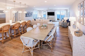 A spacious living area with a large wooden dining table, wicker chairs, and a sofa. - Beachfront 3rd-floor condo with ocean views, 3 pools, free wifi gym & w/d (Virginia Beach)