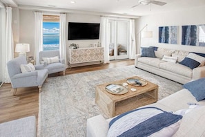 A living room with a sofa, armchairs, a coffee table, a TV, and a view of the ocean. - Beachfront 3rd-floor condo with ocean views, 3 pools, free wifi gym & w/d (Virginia Beach)