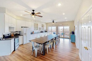 A spacious kitchen with white cabinets, a wooden dining table, and ceiling fans. - Oceanfront home with beach access, huge decks & pool table - great for groups (Virginia Beach)