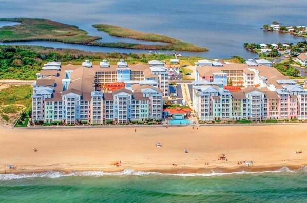 Ein Strandhotel mit mehreren Gebäuden, einem Sandstrand und Wasserflächen im Hintergrund.
