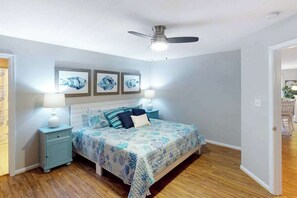 Un dormitorio con una cama, dos mesitas de noche, un ventilador de techo y una obra de arte en la pared.