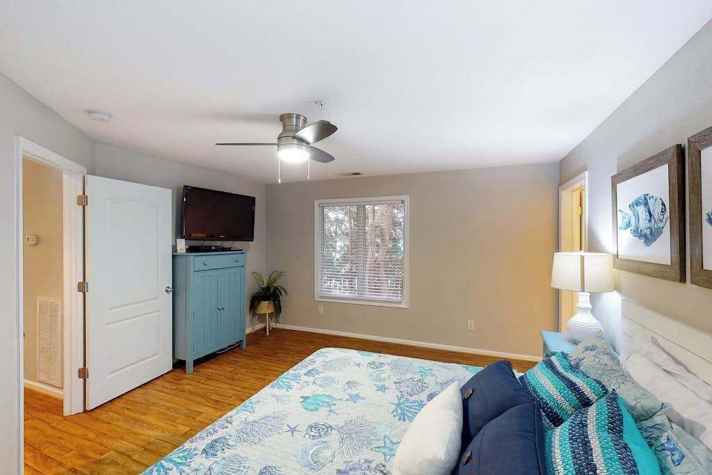 Un dormitorio con cama, ventilador de techo, televisor, ventana y puerta.