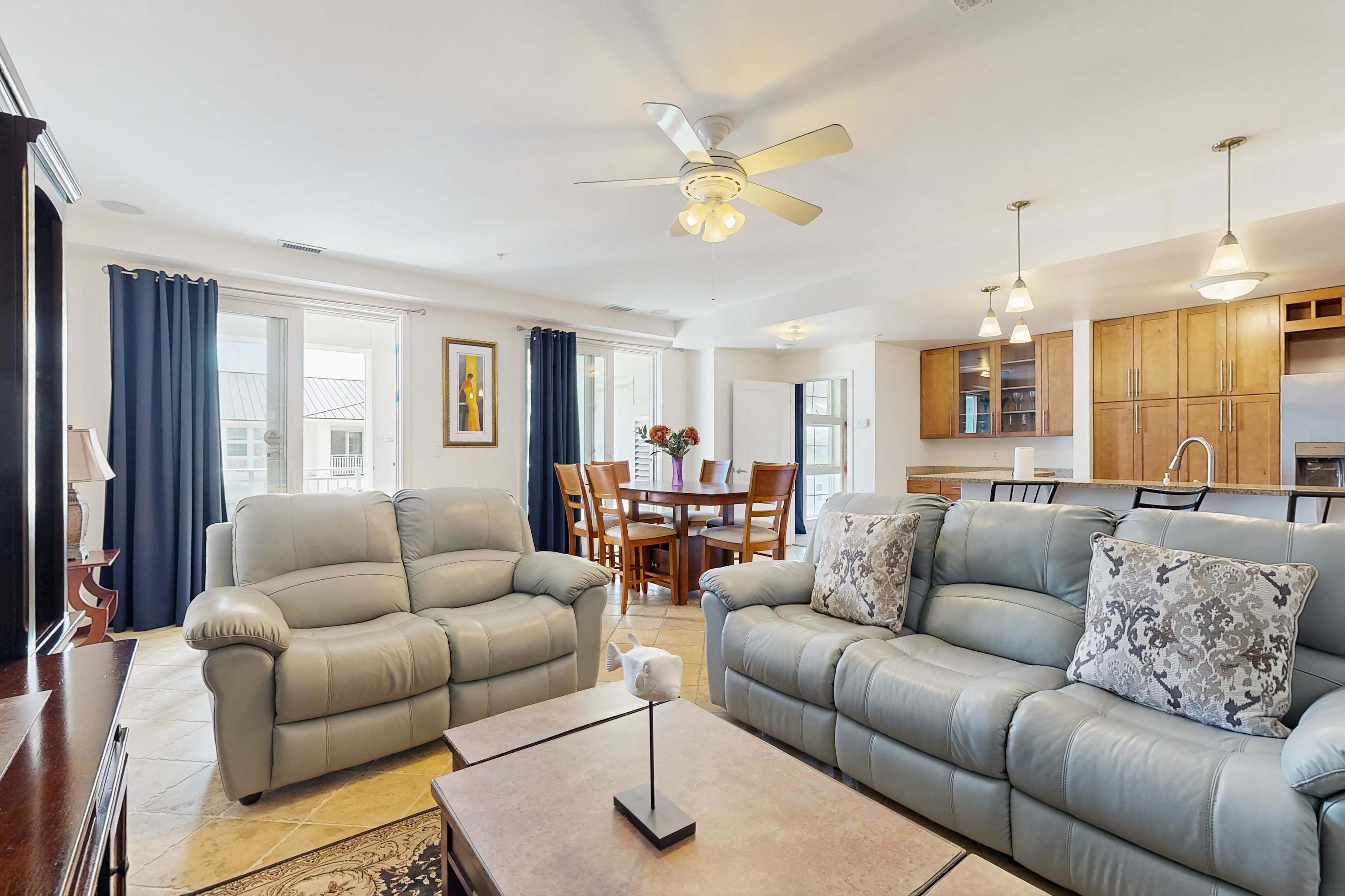 A living room with two sofas, a coffee table, a ceiling fan, and a dining area with a table and chairs.