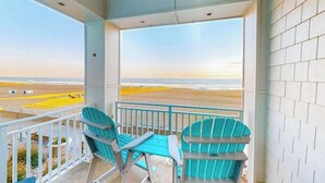 Ein Balkon mit zwei Stühlen und einem Tisch, mit Blick auf einen Strand.