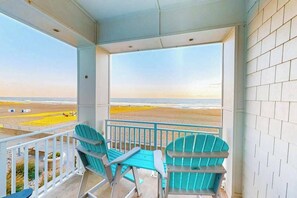 Ein Balkon mit zwei Stühlen und einem Tisch, mit Blick auf einen Strand.