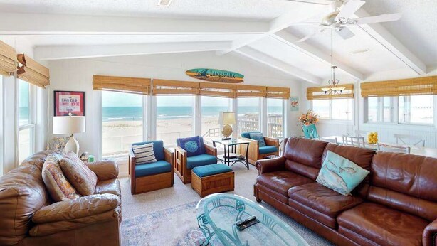 A spacious living room with a view of the ocean, furnished with leather sofas and blue chairs, and a ceiling fan. - Oceanfront home w/private pool, beautiful views, WiFi, central AC, private W/D (Virginia Beach)