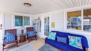 A covered porch with wooden chairs, a blue sofa, and a small table. - Oceanfront home w/private pool, beautiful views, WiFi, central AC, private W/D (Virginia Beach)