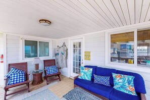 A covered porch with wooden chairs, a blue sofa, and a small table. - Oceanfront home w/private pool, beautiful views, WiFi, central AC, private W/D (Virginia Beach)