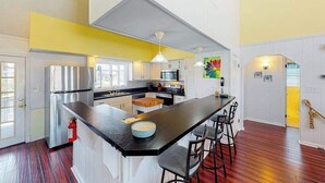 A modern kitchen with a central island, stainless steel appliances, and a bright yellow accent wall. - Wonderful home on the bay with private dock and pool, WiFi, washer/dryer (Virginia Beach)