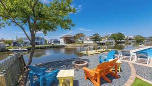 A lakeside outdoor seating area with Adirondack chairs, a fire pit, and a pool. - Wonderful home on the bay with private dock and pool, WiFi, washer/dryer (Virginia Beach)