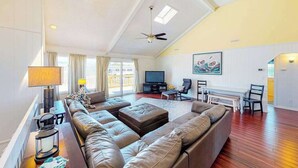 A spacious living room with a large sofa, a television, and a ceiling fan. - Wonderful home on the bay with private dock and pool, WiFi, washer/dryer (Virginia Beach)