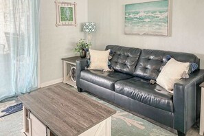 Ein Wohnzimmer mit einer Ledersofa, einem Holztisch, einem Beistelltisch mit Lampe und gerahmten Kunstwerken an den Wänden.