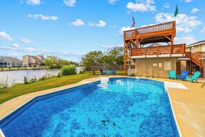 Ein Schwimmbad mit Holzterrasse, Stühlen, einer Flagge und Blick auf einen See.