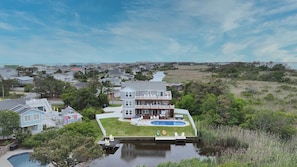 A large house with a pool, surrounded by greenery and a river.