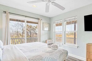 A bedroom with a bed, two windows, a ceiling fan, and a view of trees.