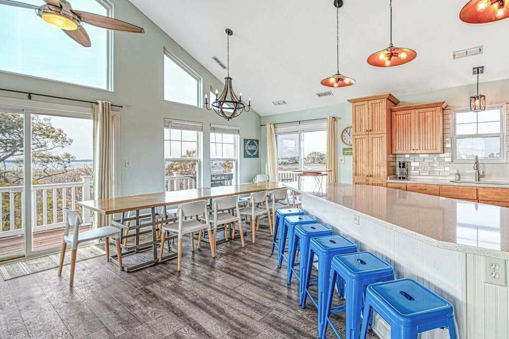 A spacious kitchen with wooden cabinets, a large island with stools, and a view through large windows.