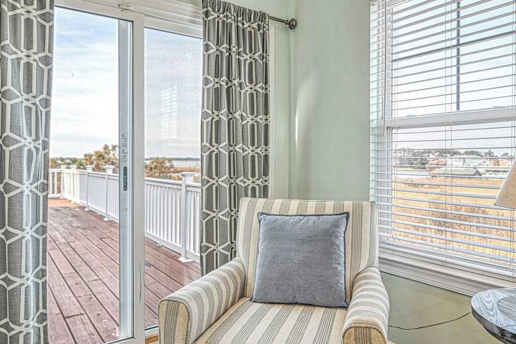 A room with a view of a balcony, a striped armchair, and a window with blinds.