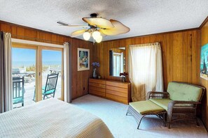 A room with a bed, a dresser, a chair, a wicker sofa, a ceiling fan, and a large window with a view. - Oceanfront home w/ocean views, WiFi, central AC, balcony, deck, washer/dryer (Virginia Beach)