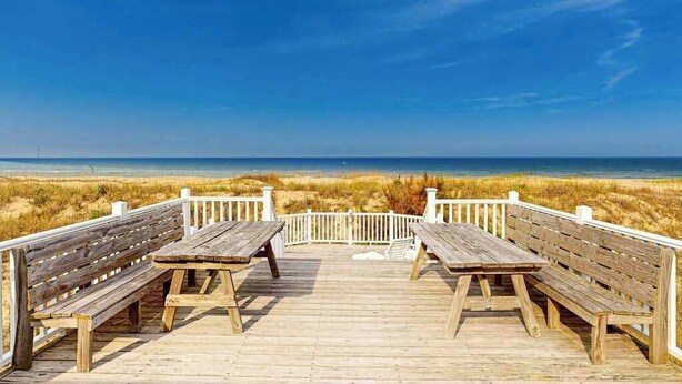 Una terraza de madera con bancos que da a una playa.