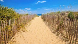 Un sendero arenoso bordeado por vallas de madera que conduce a una playa.