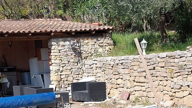 Una piscina con un muro de piedra, una planta en maceta y una gran maceta de terracota.