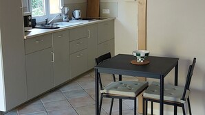 Una cocina con una mesa de comedor, sillas, un reloj colgante y una ventana con cortinas.