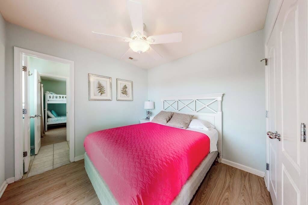 Un dormitorio con cama, ventilador de techo, puerta y pasillo que conduce a otra habitación.