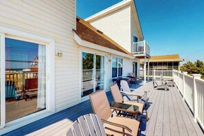 Een overdekt terras met buitenmeubilair, een glazen deur en een wit gebouw met balkon.