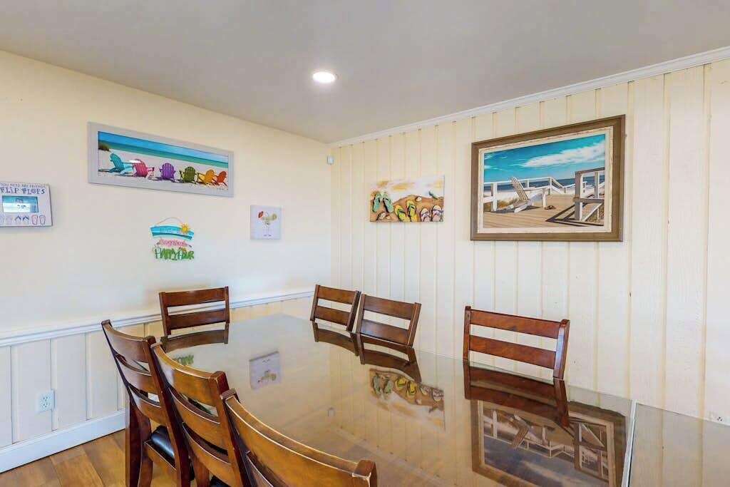 Un coin repas avec une table en verre entourée de chaises en bois, des œuvres d’art encadrées accrochées aux murs et un tableau blanc sur lequel on a écrit.