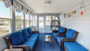 Ein Wintergarten mit Korbmöbeln, einem Glastisch und einer Wand mit dem Schild 'BEACH HOUSE RULES'.