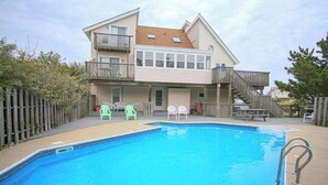 Ein zweistöckiges Gebäude mit Swimmingpool, Außenbereich und einer Holzterrasse.
