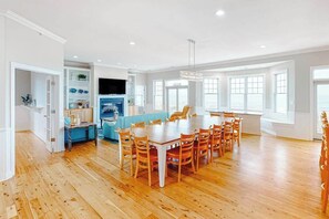 Ein großzügiger Essbereich mit einem großen Holztisch und Stühlen, eine Küche mit weißen Schränken und ein großes Fenster für natürliches Licht.