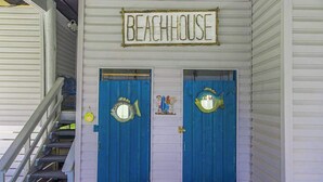 Un edificio con un cartello che riporta 'BEACHHOUSE' sopra due porte blu, ognuna con uno specchio e una piccola statua.