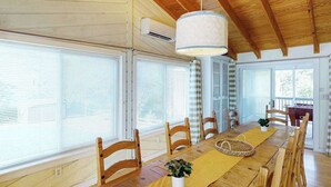 Zona pranzo con tavolo in legno, sedie, lampadario e ampie finestre.