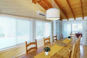 Ein Essbereich mit einem Holztisch, Stühlen, einer Pendelleuchte und großen Fenstern.