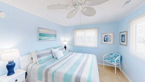 Une chambre à coucher comprenant un lit, une table de chevet, une chaise, un ventilateur de plafond et une fenêtre.